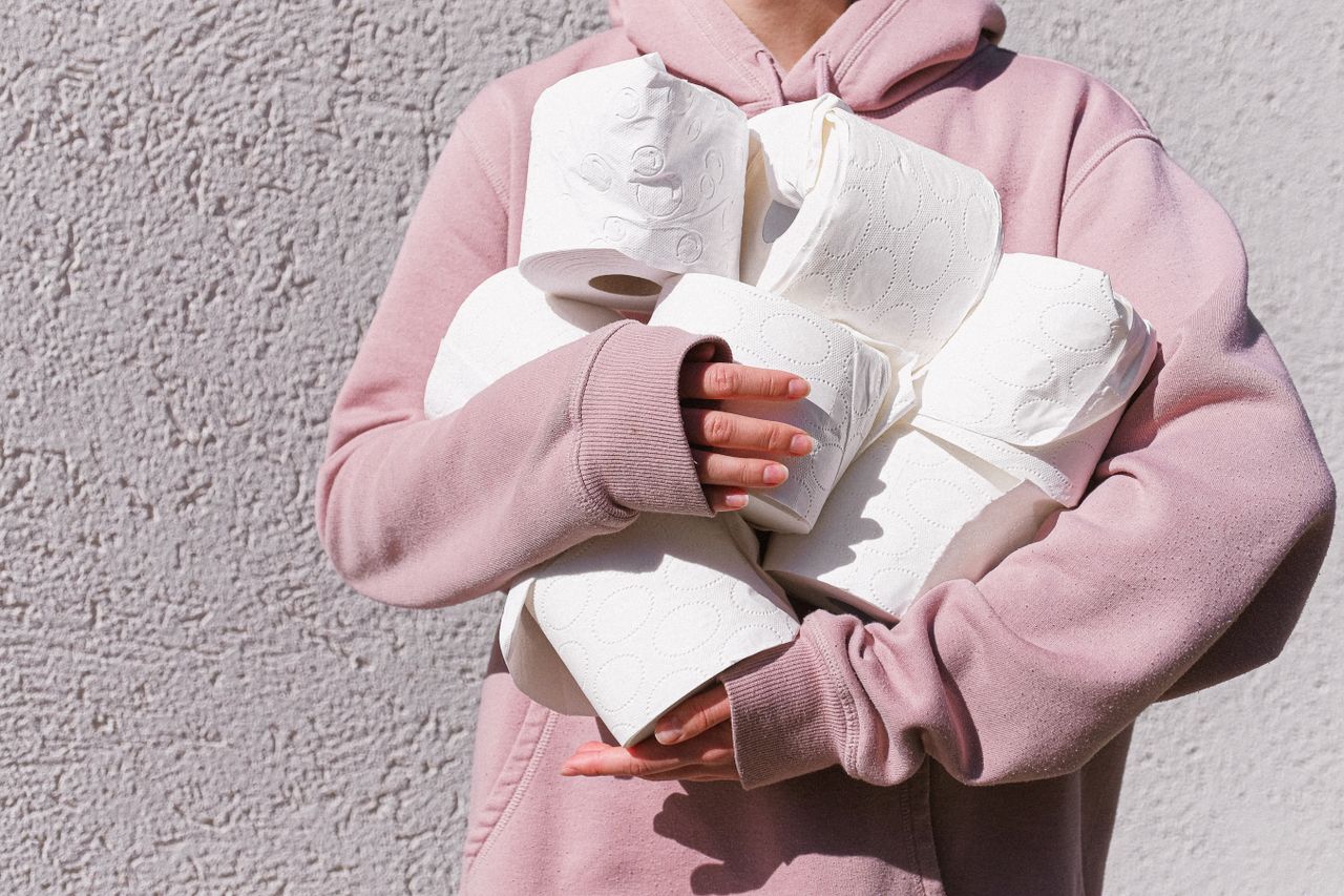 portfolio-04 A person in a pink hoodie holds multiple rolls of toilet paper against a textured wall.