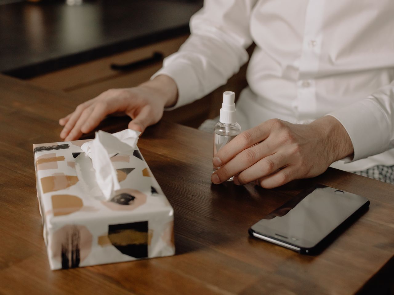 portfolio-03 A person using hand sanitizer with tissues and phone on a wooden table, promoting hygiene.